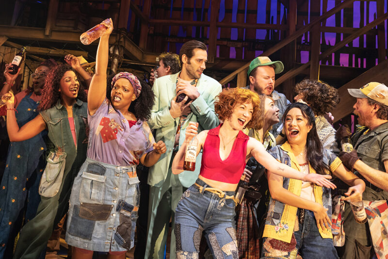 A group of a dozen people lift drinks in celebration in a barn .